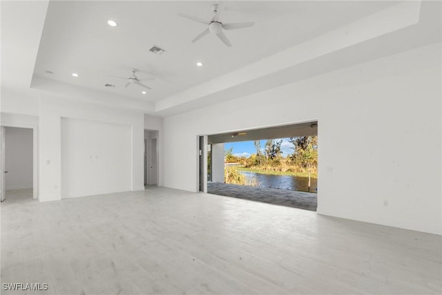 unfurnished living room featuring light wood finished floors, visible vents, a ceiling fan, a tray ceiling, and recessed lighting