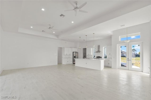 unfurnished living room featuring a tray ceiling, french doors, light wood-style flooring, a ceiling fan, and a sink