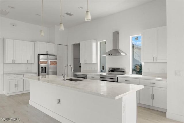 kitchen featuring wall chimney exhaust hood, sink, stainless steel appliances, a kitchen island with sink, and white cabinets