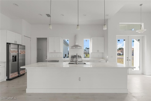 kitchen with an island with sink, wall chimney range hood, white cabinets, and stainless steel fridge with ice dispenser