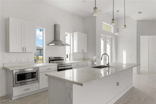 kitchen with wall chimney range hood, an island with sink, a sink, and appliances with stainless steel finishes