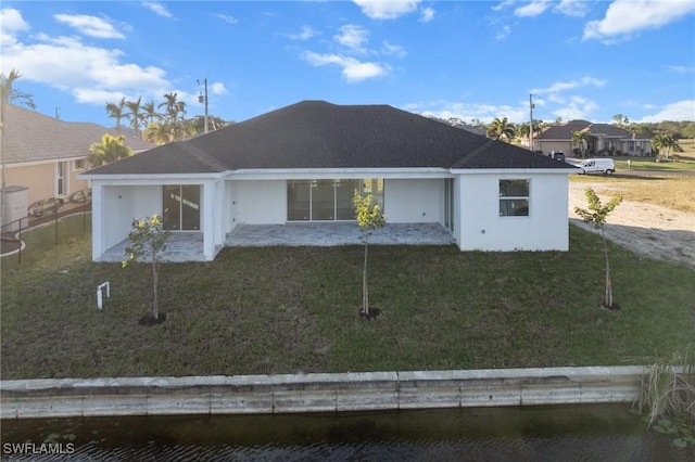 back of house with a water view, a yard, and stucco siding