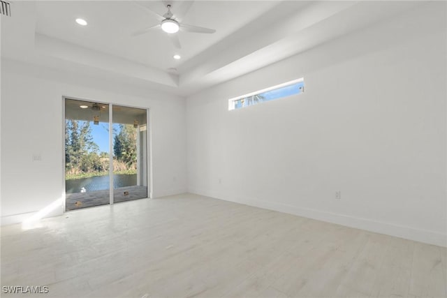 empty room featuring baseboards, a ceiling fan, a tray ceiling, light wood-type flooring, and recessed lighting