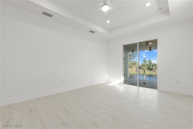 spare room with a water view, visible vents, baseboards, light wood-type flooring, and a raised ceiling