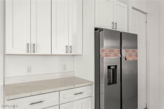 kitchen featuring stainless steel fridge, light stone counters, and white cabinets