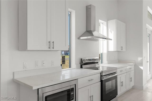 kitchen featuring white cabinets, wall chimney range hood, stainless steel appliances, and light stone countertops