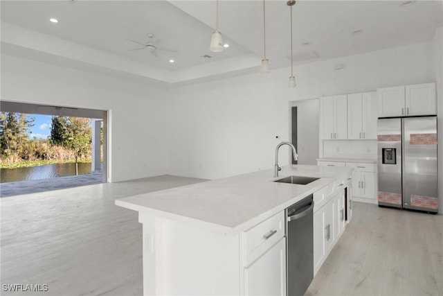 kitchen with decorative light fixtures, a center island with sink, stainless steel appliances, white cabinetry, and a sink