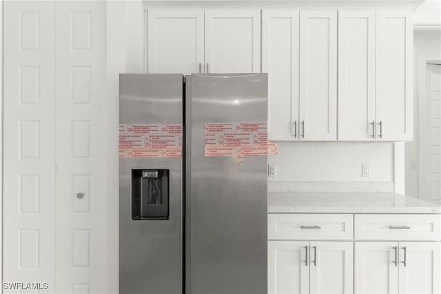 kitchen with stainless steel fridge, light stone countertops, and white cabinets