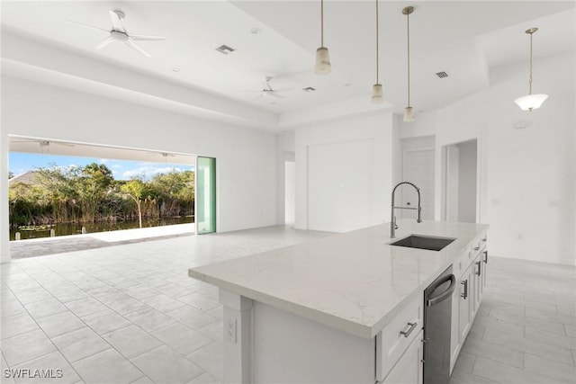 kitchen with a sink, white cabinetry, hanging light fixtures, light stone countertops, and a center island with sink