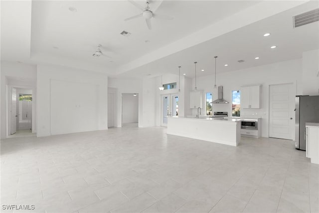 unfurnished living room featuring ceiling fan, light tile patterned flooring, sink, and a tray ceiling