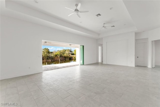 empty room featuring ceiling fan, a raised ceiling, and light tile patterned floors