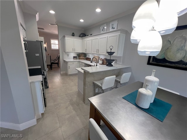 kitchen with a breakfast bar, crown molding, kitchen peninsula, pendant lighting, and white cabinets