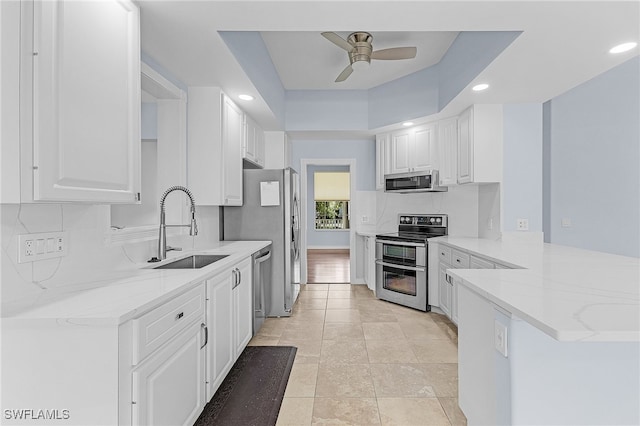 kitchen with white cabinetry, sink, stainless steel appliances, light stone counters, and kitchen peninsula