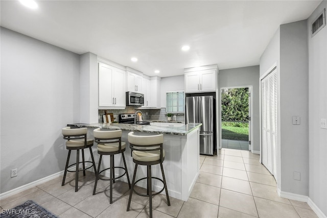 kitchen with kitchen peninsula, white cabinetry, light stone countertops, and appliances with stainless steel finishes