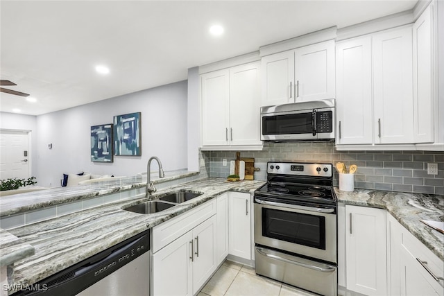 kitchen featuring light stone countertops, appliances with stainless steel finishes, sink, light tile patterned floors, and white cabinetry