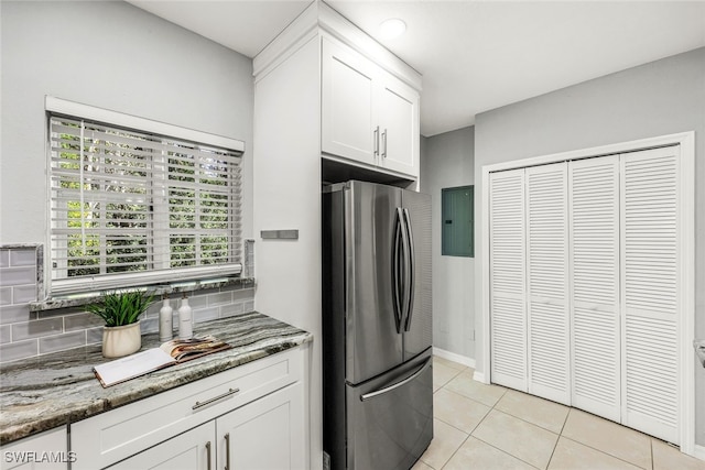 kitchen featuring stainless steel fridge, tasteful backsplash, dark stone counters, light tile patterned floors, and white cabinets