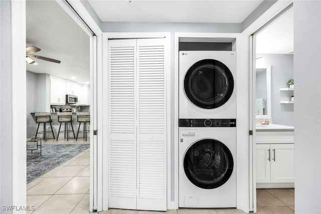 clothes washing area featuring ceiling fan, stacked washing maching and dryer, and light tile patterned floors