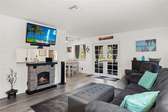 living room featuring french doors, hardwood / wood-style flooring, a stone fireplace, and ceiling fan