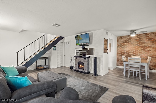 living room with ceiling fan, a fireplace, brick wall, and hardwood / wood-style flooring