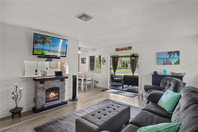 living room featuring a textured ceiling, ceiling fan, light wood-type flooring, and a fireplace