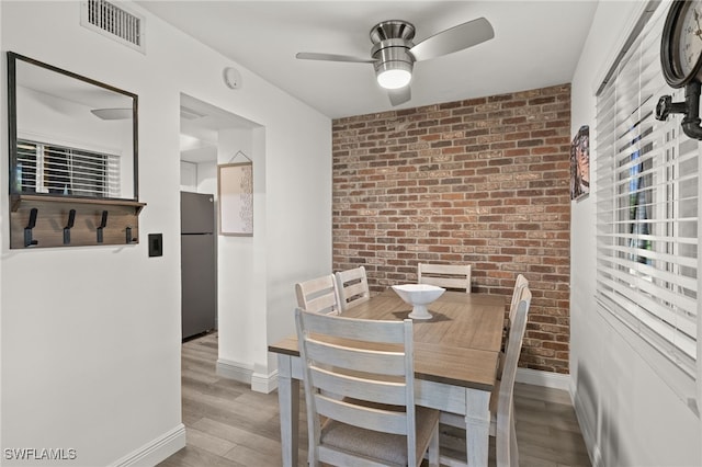 dining area featuring ceiling fan, light wood-type flooring, and brick wall