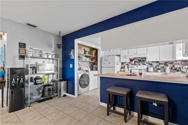 kitchen with white appliances, white cabinets, a kitchen breakfast bar, light tile patterned floors, and washer / clothes dryer