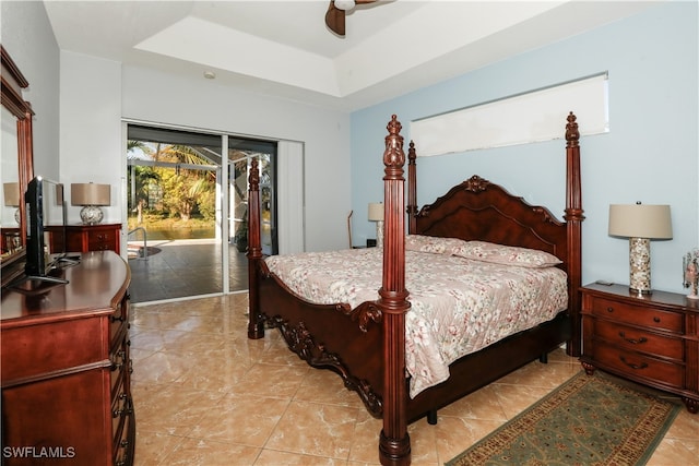 bedroom with ceiling fan, access to exterior, and a tray ceiling