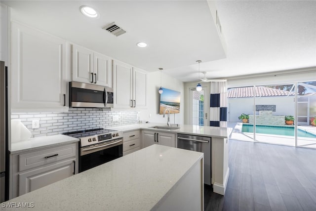 kitchen with sink, white cabinets, stainless steel appliances, and decorative light fixtures