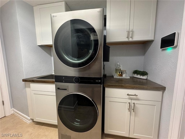 clothes washing area with stacked washing maching and dryer, cabinets, and light tile patterned flooring