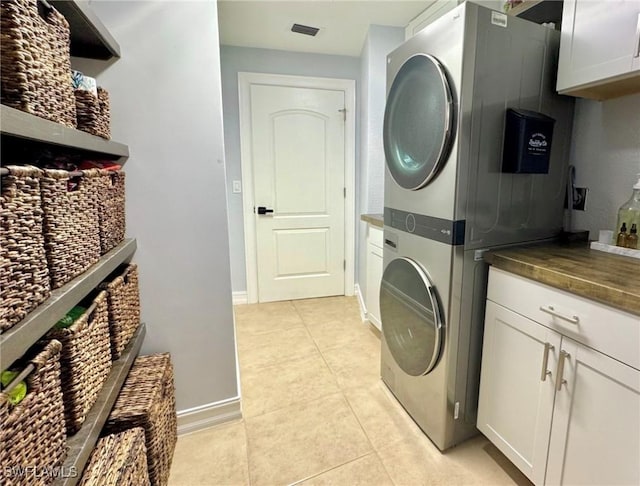 laundry room with cabinets, light tile patterned floors, and stacked washing maching and dryer