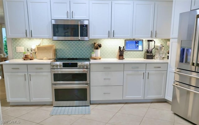 kitchen with appliances with stainless steel finishes, light tile patterned floors, white cabinets, and backsplash