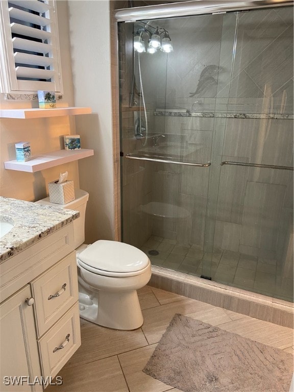 bathroom featuring tile patterned flooring, vanity, toilet, and a shower with door