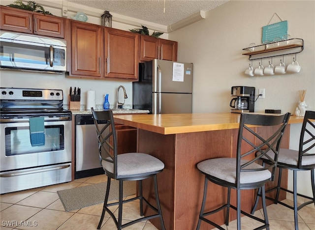 kitchen with wood counters, a breakfast bar, a textured ceiling, stainless steel appliances, and light tile patterned floors