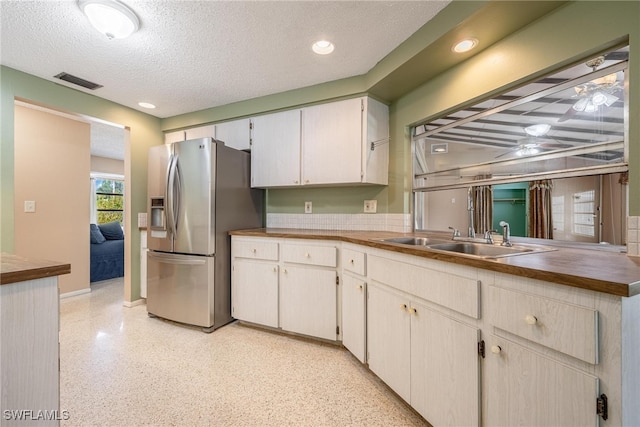 kitchen featuring white cabinetry, sink, ceiling fan, stainless steel fridge, and a textured ceiling