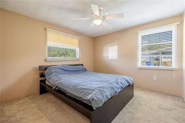 bedroom with a textured ceiling, light colored carpet, multiple windows, and ceiling fan