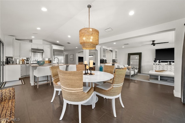 dining space with ceiling fan with notable chandelier, sink, lofted ceiling, and dark wood-type flooring