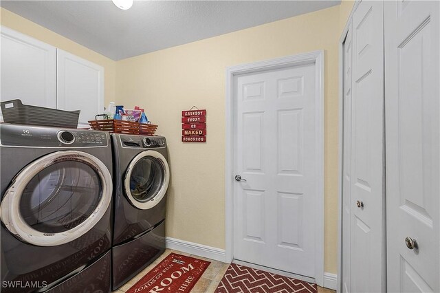 clothes washing area featuring cabinets, tile patterned floors, and washing machine and clothes dryer