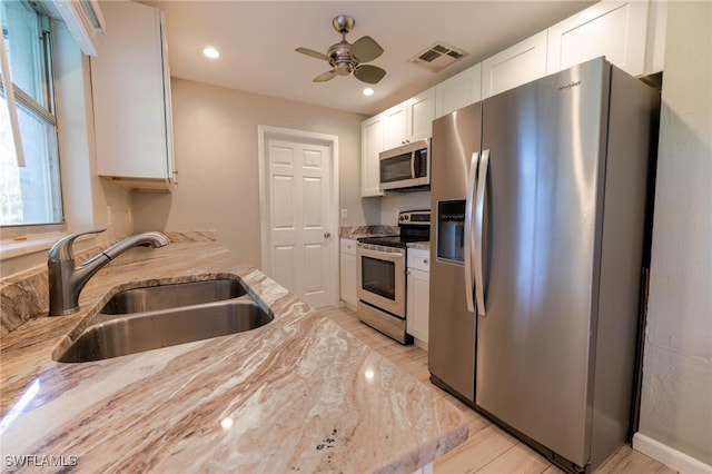 kitchen with light stone countertops, appliances with stainless steel finishes, white cabinetry, and sink