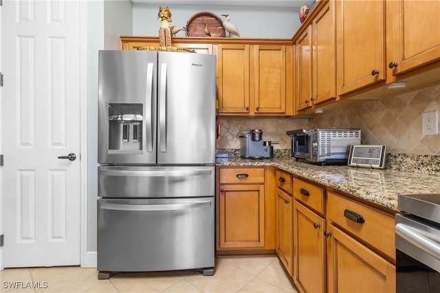 kitchen featuring light stone counters, light tile patterned floors, tasteful backsplash, and stainless steel refrigerator with ice dispenser