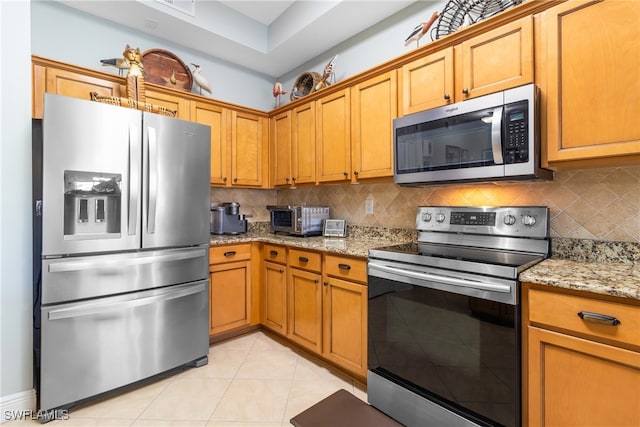 kitchen featuring tasteful backsplash, light stone countertops, appliances with stainless steel finishes, and light tile patterned flooring