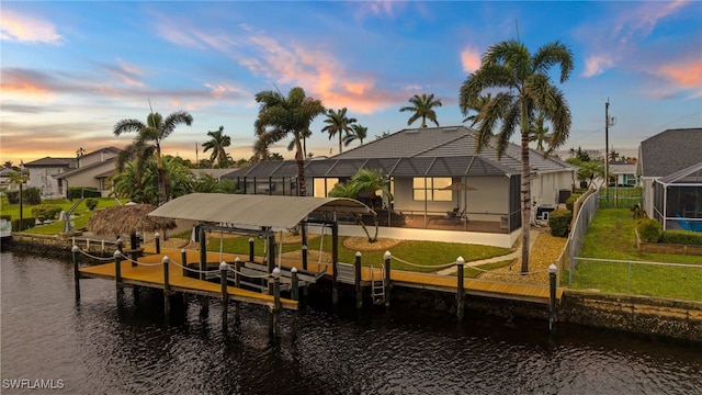 dock area featuring a water view, a lawn, and a lanai