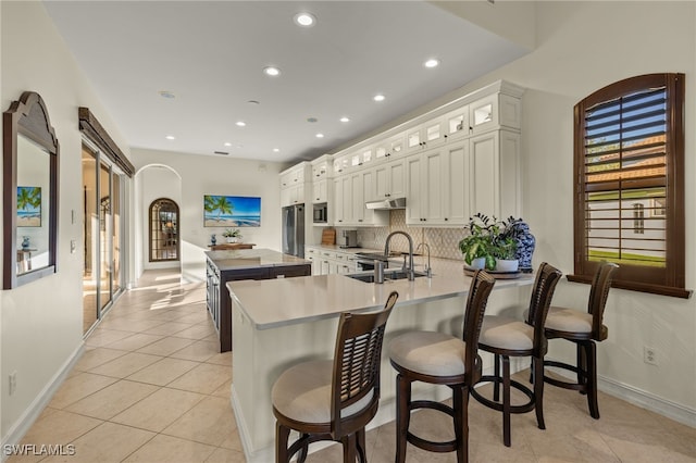 12656 Grandezza Cir, Estero, FL 33928 - kitchen with a kitchen island, light tile patterned flooring, light countertops, glass insert cabinets, and a peninsula