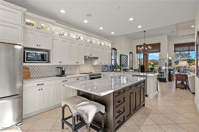 kitchen featuring pendant lighting, white cabinets, a kitchen island, light stone counters, and stainless steel appliances