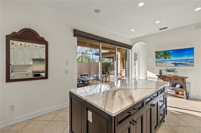 kitchen with decorative backsplash, light stone counters, dark brown cabinets, light tile patterned floors, and a kitchen island