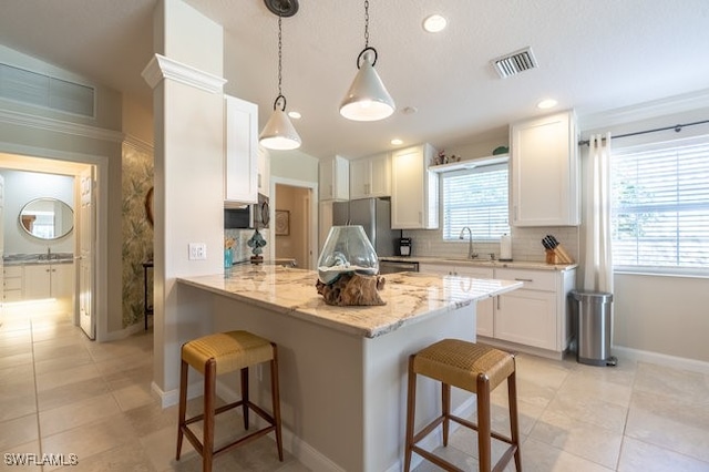 kitchen featuring stainless steel fridge, a kitchen breakfast bar, pendant lighting, light tile patterned floors, and white cabinets