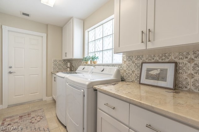 laundry area featuring washing machine and dryer, light tile patterned flooring, and cabinets