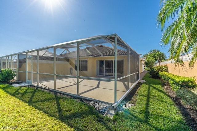 rear view of house featuring glass enclosure and a lawn