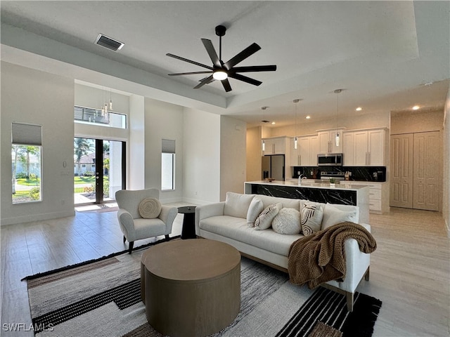 living room with ceiling fan with notable chandelier, french doors, a tray ceiling, and light hardwood / wood-style flooring