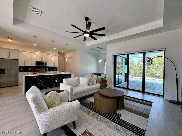 living room with a raised ceiling, ceiling fan, and light wood-type flooring