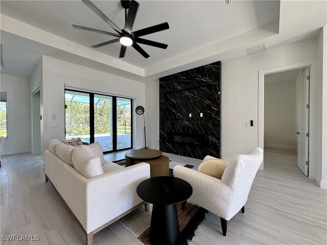 living room with ceiling fan, a raised ceiling, and light hardwood / wood-style flooring